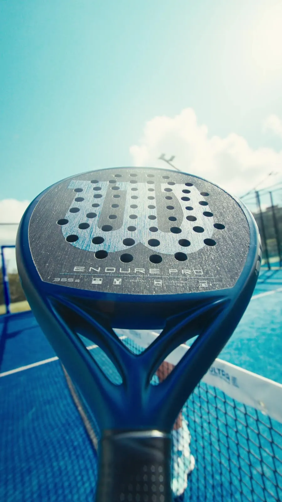 Gros plan sur une raquette de padel Wilson de la nouvelle gamme, terrain bleu en arrière-plan